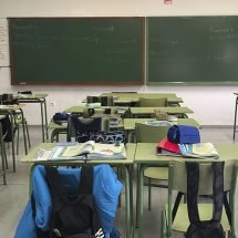 Mesas de un colegio con mochilas en los asientos y una pizarra al final.