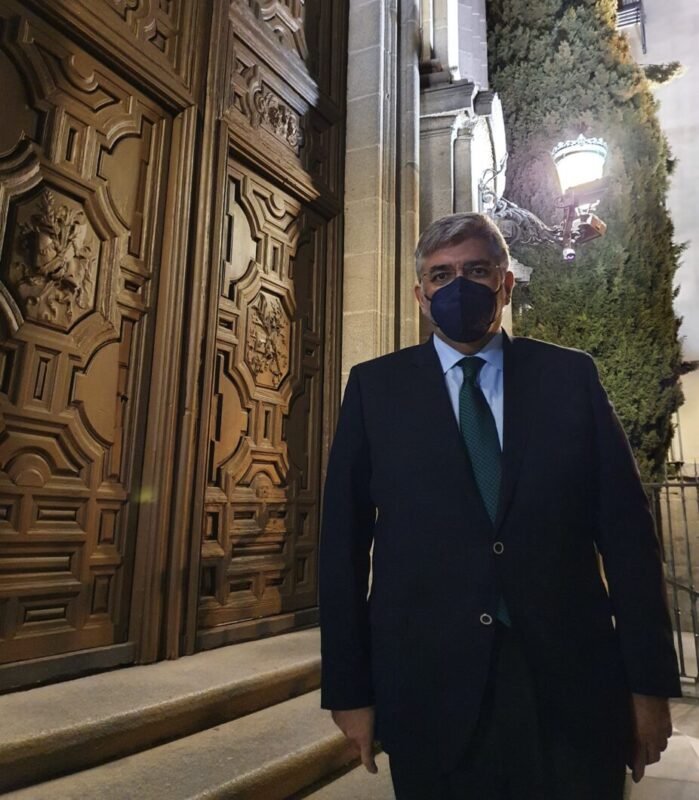 El Hermano Mayor de las Hermandad de los Estudiantes de Madrid, vestido con traje y corbata, frente a la puerta de la Basílica Pontificia de San Miguel.