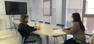 Entrevistada y periodista hablan en una sala. Sentadas frente a frente en una mesa con distancia de seguridad y mascarillas.