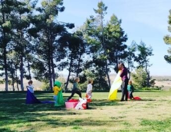 Cinco niños realizando aprendizaje experimental en un prado rodeado de árboles junto a su mamá de día