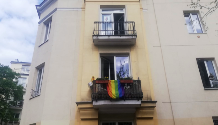 Balcón con la bandera LGTBI+ colgada en un edificio amarillo clásico en Varsovia.