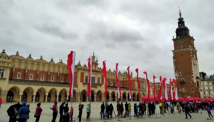 Cola para la vacunación de la COVID-19 en la Plaza del Mercado de Cracovia con el edificio del mercado de fondo y banderas de Polonia decorando la plaza.