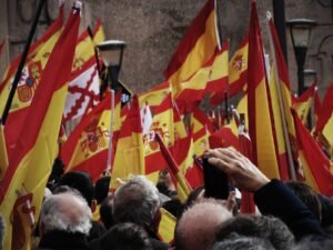 Imagen de banderas de España elevadas por las personas en una manifestación, en la parte inferior se recortan las cabezas de las personas que aguantan las banderas.