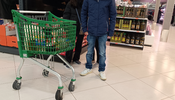 Carro de la compra a medio llenar colocado frente a la estantería del aceite en un supermercado español acompañado de una familia